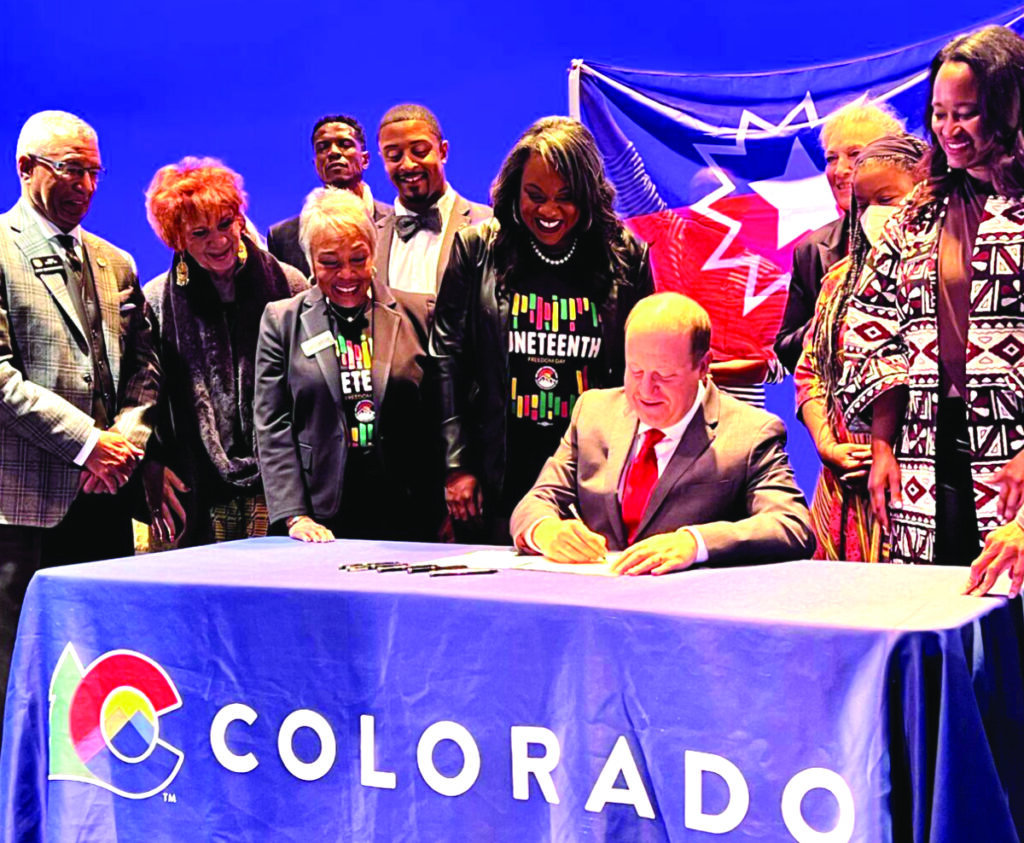 Colorado Gov. Jared Polis, seated and surrounded by supporters, signs legislation making Juneteenth a state holiday during a signing ceremony in Denver in May. Photo credit: Lens of Ansar