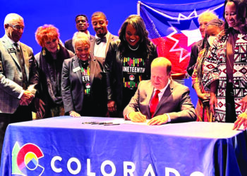 Colorado Gov. Jared Polis, seated and surrounded by supporters, signs legislation making Juneteenth a state holiday during a signing ceremony in Denver in May. Photo credit: Lens of Ansar