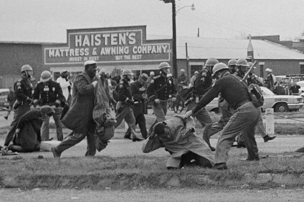 FILE - An Alabama state trooper swings a club at John Lewis, right foreground, then chairman of the Student Nonviolent Coordinating Committee, to break up a civil rights voting march in Selma, Ala., March 7, 1965. On Sunday, March 5, 2023, President Joe Biden is set to pay tribute to the heroes of “Blood Sunday," joining thousands for the annual commemoration of the seminal moment in the civil rights movement that led to passage of landmark voting rights legislation nearly 60 years ago. Photo credit: file photo, The Associated Press