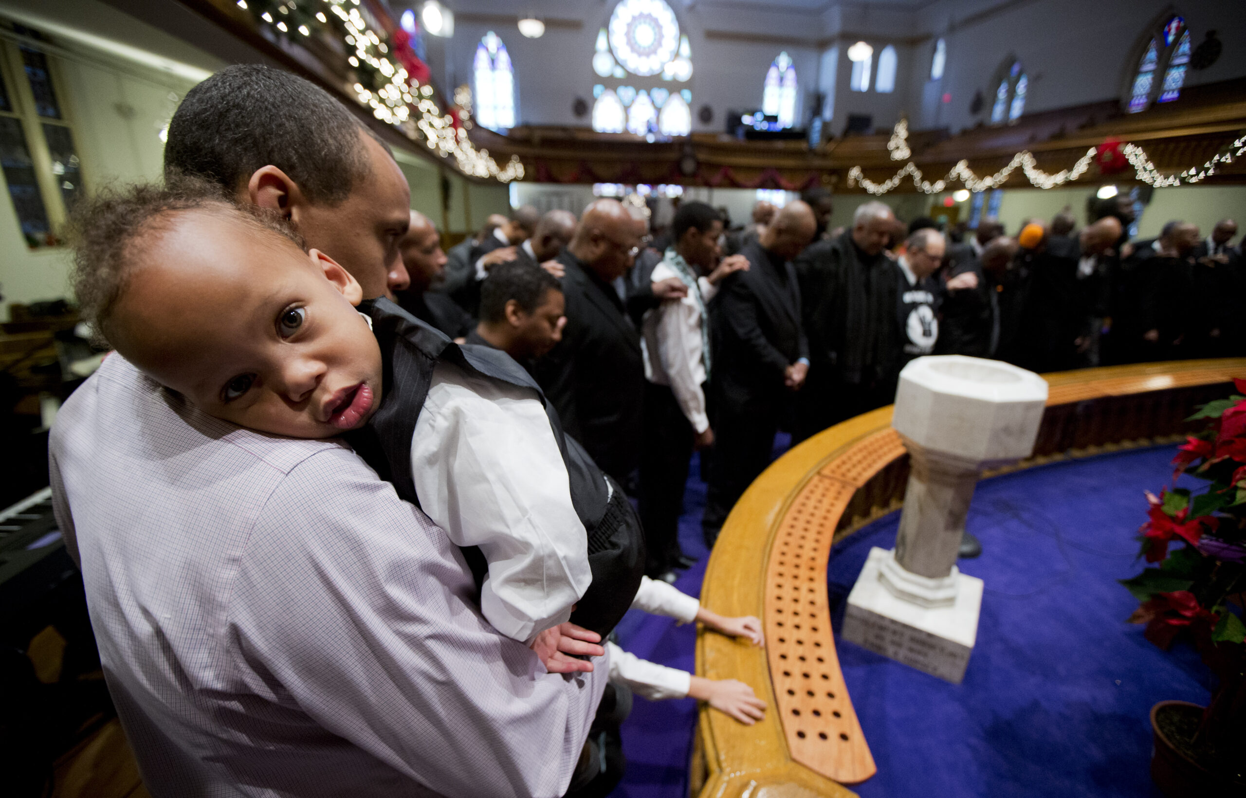 Antonio Harrison III, 2, rests in the arms of his father, Antonio Harrison Jr., as male churchgoers gather in front of the altar during service at the African Methodist Episcopal Church in Washington, D.C., Sunday, Dec. 14, 2014. Photo credit: Manuel Balce Ceneta, The Associated Press