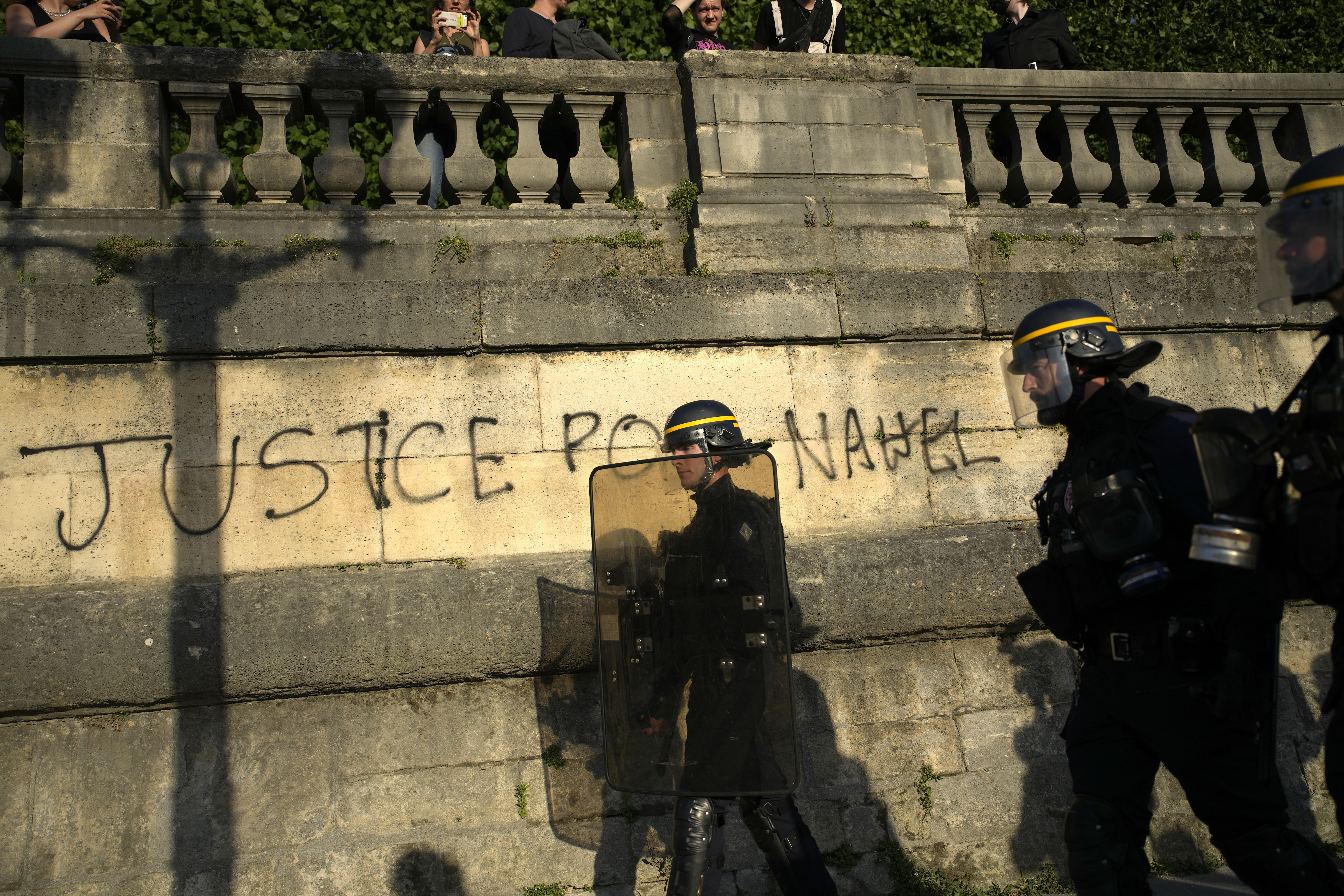 Police patrol as youths gather on Concorde square during a protest in Paris, France, Friday, June 30, 2023. French President Emmanuel Macron urged parents Friday to keep teenagers at home and proposed restrictions on social media to quell rioting spreading across France over the fatal police shooting of a 17-year-old driver. Writing on wall reads in French "Justice for Nahel" Photo credit: Lewis Joly, The Associated Press