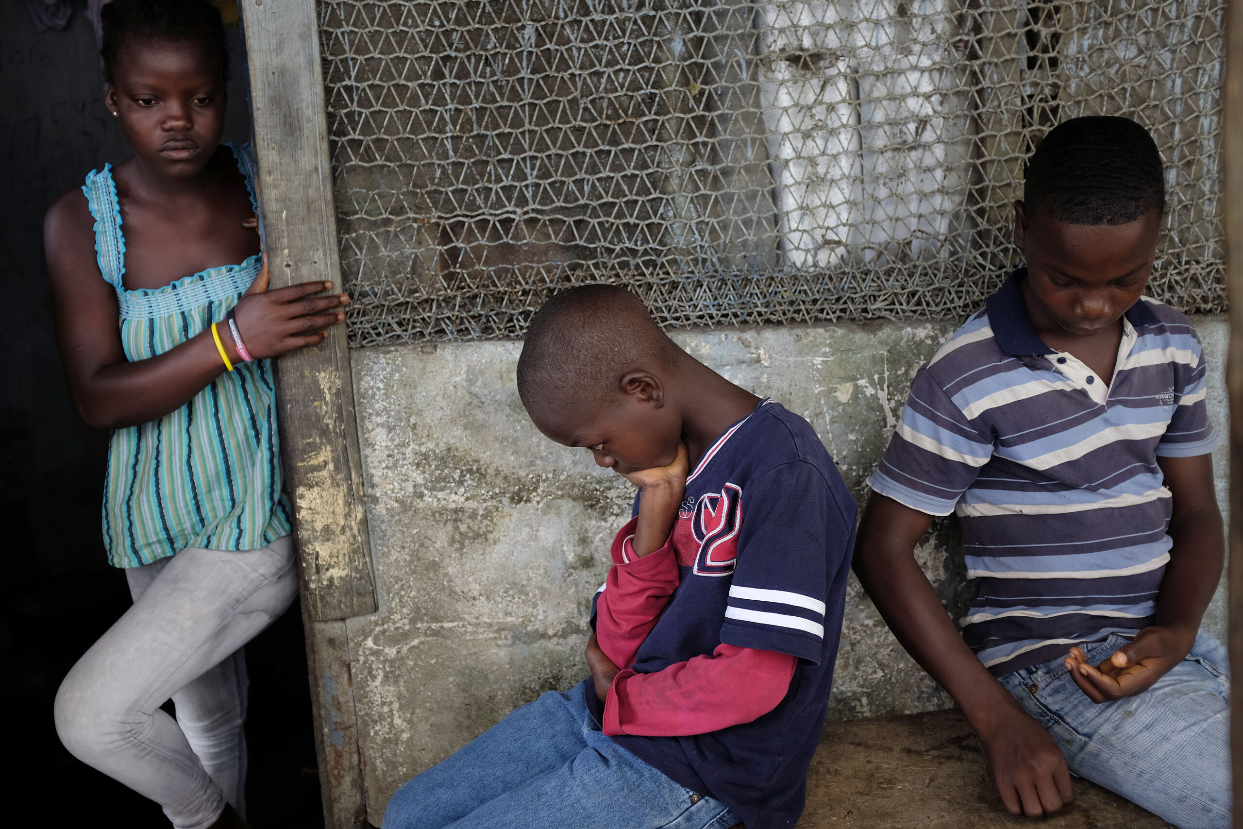 In this photo taken Sunday Sept. 28, 2014, Promise, 16, Emmanuel Junior, 11, and Benson, 15, Cooper sit at their St. Paul Bridge home in Monrovia, Liberia. The Cooper children are now orphans, having lost their mother, Princess, in July, and their father Emmanuel in August to Ebola. Their 5-month-old baby brother, Success, also succumbed to the virus in August. Ruth, their 13-year-old sister is being hospitalized with Ebola. Liberia's current crisis involving street children is partly due to the ravaging effects that Ebola had on the country nearly a decade ago. Photo credit: Jerome Delay, the Associated Press.