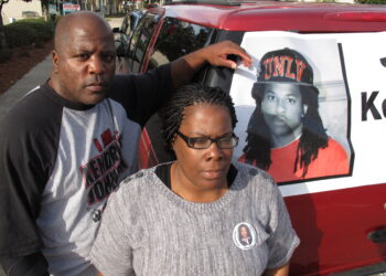 Kenneth and Jacquelyn Johnson stand next to a banner on their SUV showing their late son, Kendrick Johnson, on Dec. 13, 2013, in Valdosta, Georgia. A Georgia sheriff who last year reopened an investigation into the 2013 death of Kendrick Johnson, a teenager found inside a rolled up gym mat at school, concluded, Wednesday, Jan. 26, 2022, there was no evidence of foul play after reviewing voluminous evidence collected by federal investigators. Photo credit: Russ Bynum, The Associated Press