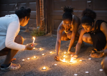 Sandriana McBroom, right, and Makhiya Mcbroom, center, light candles that spell out "RIP Kiya" at a vigil held Friday, Aug. 25, 2023, in Columbus, Ohio, for their friend, Ta'Kiya Young, 21, who was shot and killed a day earlier by Blendon Township police outside an Ohio supermarket. Young was pregnant and due to give birth in November, according to her family. Photo credit: Courtney Hergesheimer, The Columbus Dispatch via The Associated Press