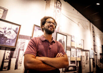 Blair-Caldwell African American Research Library’s Dexter Nelson II. He’s the museum and archives supervisor, with ideas and plans for building out context and nuance in he library’s collections on the second and third floor of the facility. Photographed Sept. 12, 2023, with a display of historic photographs from the Five Points neighborhood, where the library is situated. Photo credit: CPR News