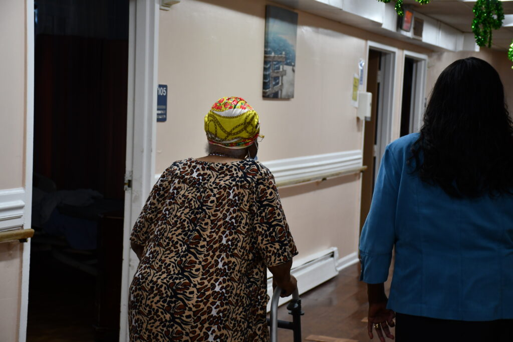 This image has an empty alt attribute; its file name is Nursing-home-resident-1024x683.jpg
One of the 29 Maryland Baptist Aged Home residents makes her way down the hall to her room in the one-story building that she and others who live there call home. To the resident's right is administrator Johana Walburn. Photo credit: B. Denise Jackson