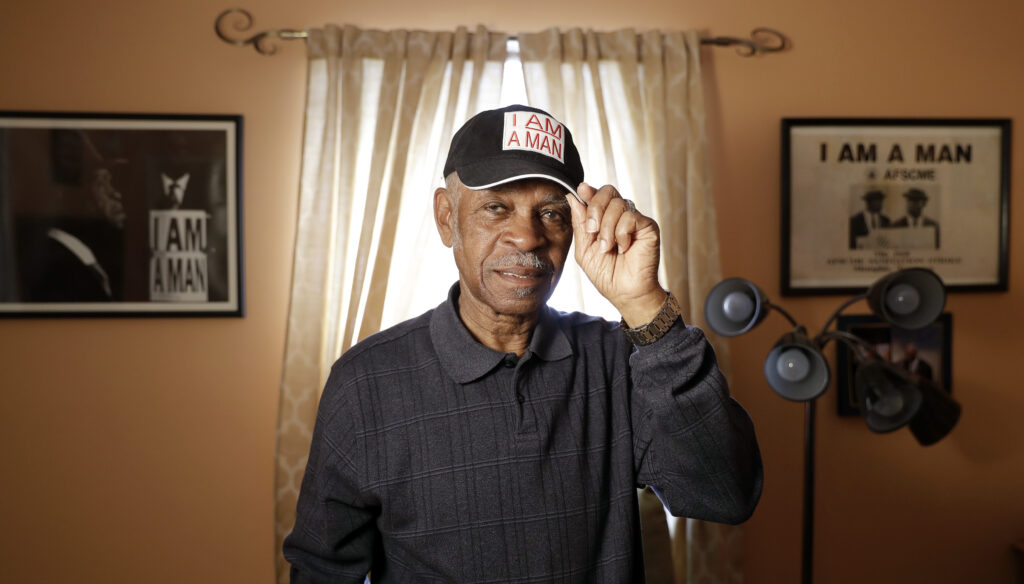 Sanitation worker Elmore Nickleberry wears a cap with the slogan "I AM A MAN" in a room in his home that displays items commemorating the civil rights movement on March 15, 2018, in Memphis, Tennessee. Nickleberry, a longtime Memphis sanitation worker who participated in the pivotal 1968 strike that brought the Rev. Martin Luther King to the city where the civil rights leader was killed, died Saturday, Dec. 30, 2023, in Memphis, according to an obituary by R.S. Lewis and Sons Funeral Home. He was 92. Photo credit: Mark Humphrey, The Associated Press