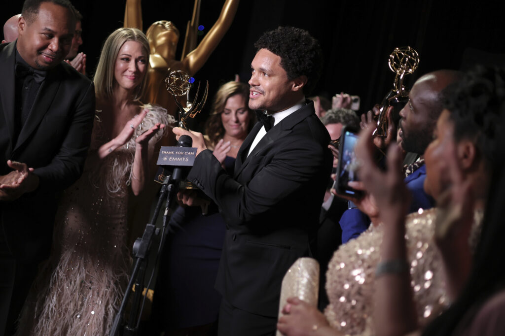 Trevor Noah, center, winner for Outstanding Talk Series, speaks backstage at the 75th Emmy Awards on Monday, Jan. 15, 2024, at the Peacock Theater in Los Angeles. Photo credit: John Salangsang, Invision for the Television Academy/The Associated Press