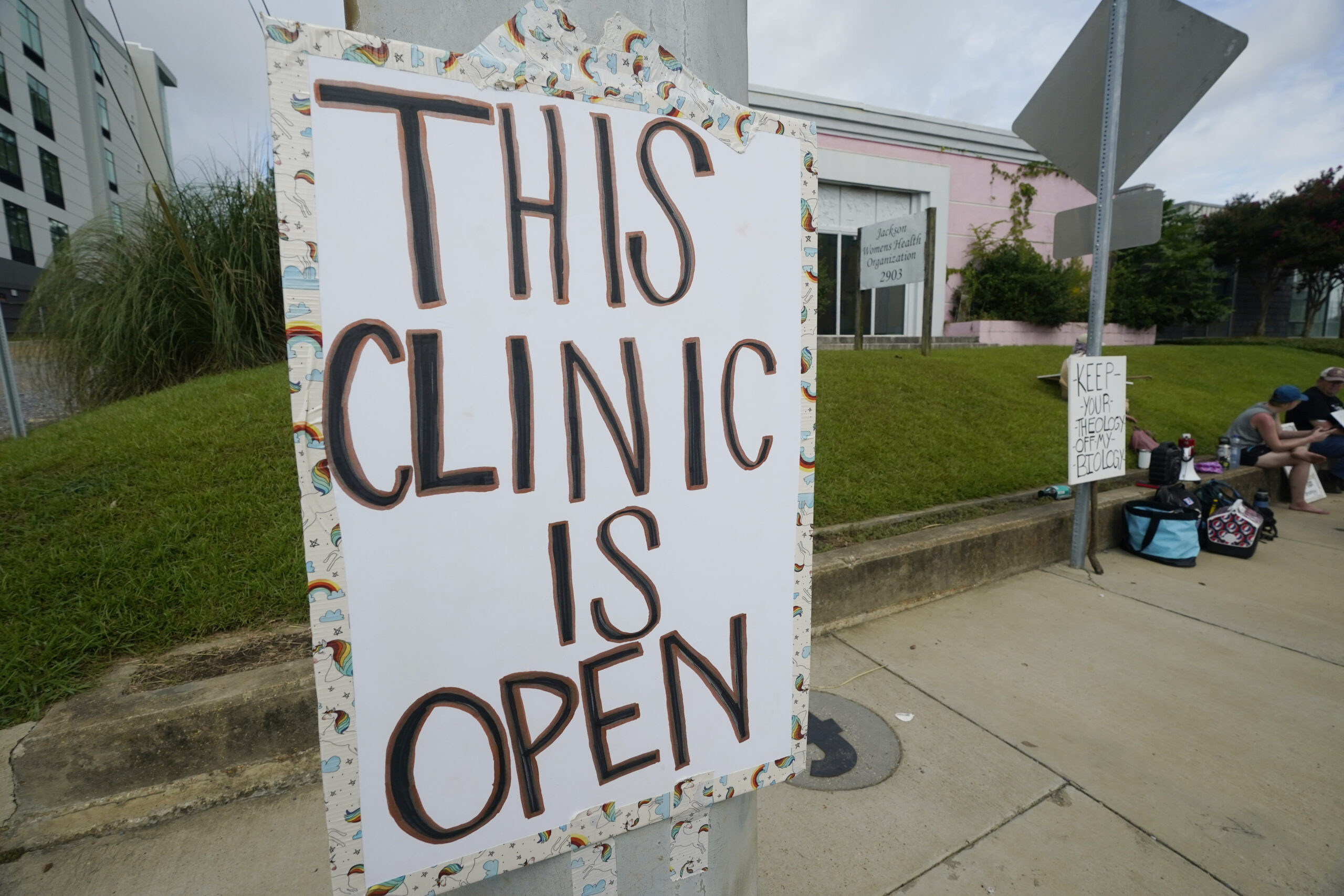 A posted sign outside the Jackson Women's Health Organization clinic assures potential patients that it is open, Sunday, July 3, 2022, in Jackson, Mississippi. The clinic is the only facility that performs abortions in the state. On June 24, 2022, the U.S. Supreme Court overturned Roe v. Wade, ending constitutional protections for abortion. Photo credit: Rogelio V. Solis, The Associated Press