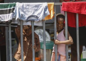Children look through a fence at a shelter for families displaced by gang violence in Port-au-Prince, Haiti, Wednesday, March 13, 2024. Photo credit: Odelyn Joseph, The Associated Press