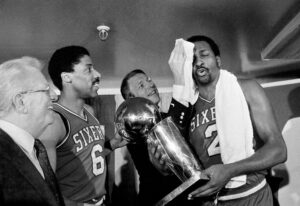Philadelphia 76ers' coach Billy Cunningham wipes the victorious brow of Moses Malone, holding the team's NBA World Championship trophy after winning game against the Los Angeles Lakers in Los Angeles, June 1, 1983. To the left is 76ers Julius Erving. Photo credit: The Associated Press