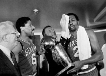 Philadelphia 76ers' coach Billy Cunningham wipes the victorious brow of Moses Malone, holding the team's NBA World Championship trophy after winning game against the Los Angeles Lakers in Los Angeles, June 1, 1983. To the left is 76ers Julius Erving. Photo credit: The Associated Press