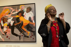 Late artist Faith Ringgold talks about her artwork in front of her painting, "Die (1967)" during a press preview of her exhibition, "American People, Black Light: Faith Ringgold's Paintings of the 1960s" at the National Museum of Women in the Arts in Washington, D.C., on June 19, 2013. Ringgold, an award-winning author and artist who broke down barriers for Black female artists and became famous for her richly colored and detailed quilts combining painting, textiles and storytelling, died Friday, April 12, 2024, at her home in Englewood, New Jersey. She was 93. Photo credit: Jacquelyn Martin, The Associated Press