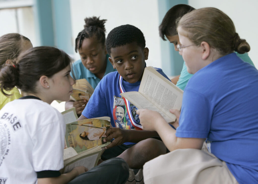 Joseph Webb, center, Kristina Carr, right, and Kaelyn Korovich, left, read outside their classroom at Air Base Elementary School, June 4, 2009, in Homestead, Florida. The school was one of the first in Miami-Dade County to integrate Black students. Friday, May 17, 2024, marks 70 years since the U.S. Supreme Court ruled that separating children in schools by race was unconstitutional. On paper, Brown v. Board of Education still stands. In reality, school integration is all but gone, the victim of a gradual series of court cases that slowly eroded it, leaving little behind. Photo credit: Wilfredo Lee, The Associated Press