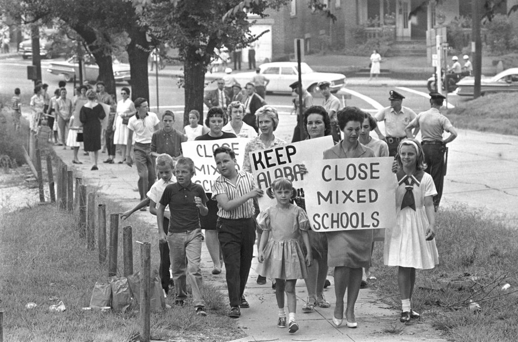 Mothers carrying protest signs accompany their children to Graymont Elementary School in Birmingham, Alabama, which was opened on an integrated basis, Sept. 4, 1963. Friday, May 17, 2024, marks 70 years since the U.S. Supreme Court ruled that separating children in schools by race was unconstitutional. On paper, Brown v. Board of Education still stands. In reality, school integration is all but gone, the victim of a gradual series of court cases that slowly eroded it, leaving little behind. Photo credit: The Associated Press