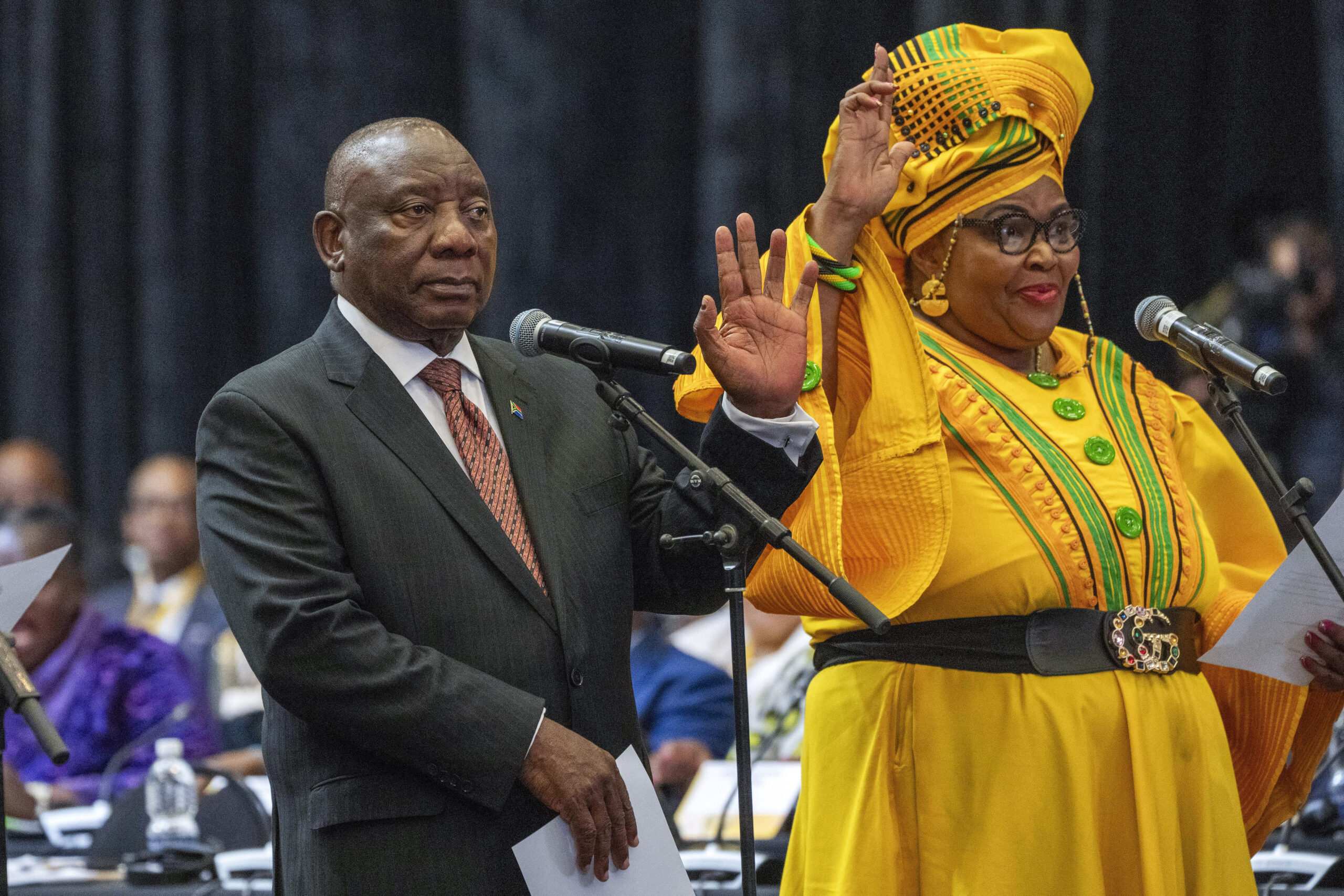 South African président Cyril Ramaphosa raises his hand as he is sworn is as a member of Parliament ahead of the vote by lawmakers to reelect him as leader of the country in Cape Town, South Africa, Friday, June 14, 2024. At right is Pemmy Majodina, an ANC lawmaker. Photo credit: Jerome Delay, The Associated Press