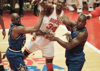 Then-Houston Rockets center Hakeem Olajuwon (34) passes the ball as he is pressured by Then-Orlando Magic players Shaquille O'Neal (32) and Horace Grant (54) during the second quarter of Game 3 of the NBA Finals at Houston on June 11, 1995. Photo credit: Rick Bowmer, The Associated Press