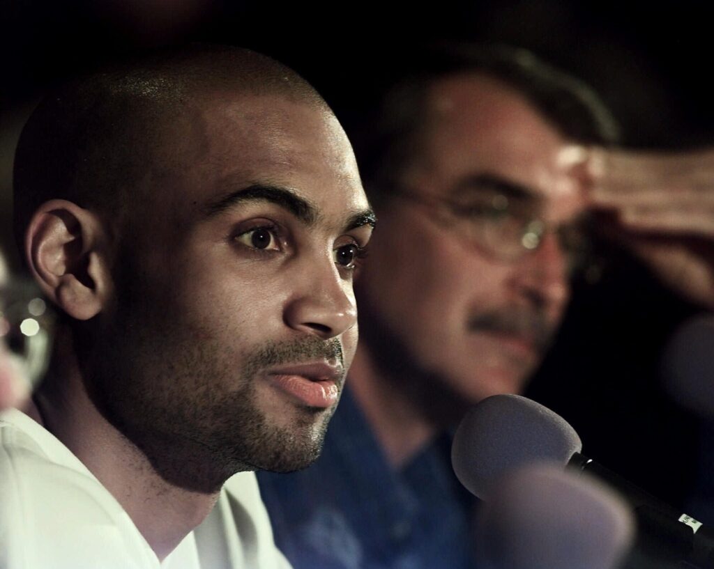 Then Detroit Piston Grant Hill, left, answers questions during a news conference as head coach George Irvine listens Wednesday, April 26, 2000, in Auburn Hills, Michigan. Hill fractured his left ankle the day before at Miami. Photo credit: Duane Burleson, The Associated Press