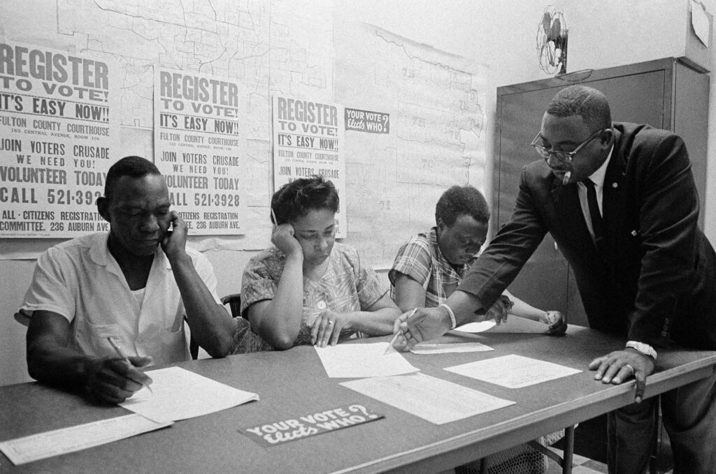 The Rev. Fred C. Bennette Jr., a civil rights movement organizer, right, instructs Black people in Atlanta how to fill out registration forms in 1963. Photo credit: Horace Cort/The Associated Press