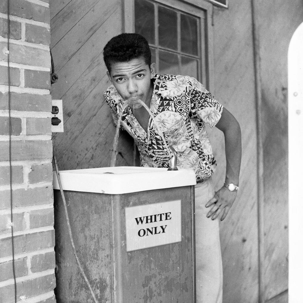 Coming back from a 1956 trip photographing South Carolina’s segregated beaches for Jet magazine, Cecil Williams stops at a filling station, closed at the time, and drinks from a “WHITE ONLY” water fountain. Image captured by Rendall Harper, a friend of the photographer. Photo courtesy of the National Endowment for the Humanities