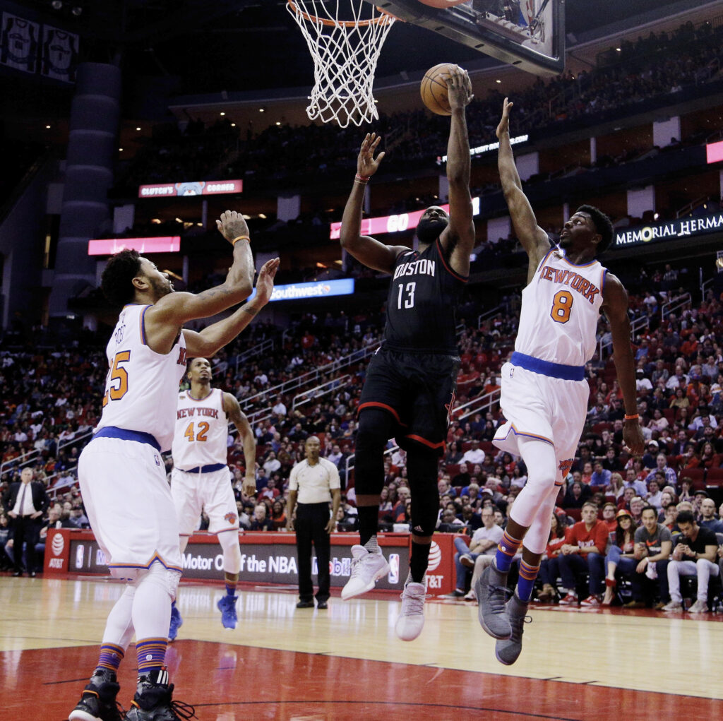 Houston Rockets guard James Harden (13) drives between New York Knicks guards Justin Holiday (8) and Derrick Rose (25) for a layup during the second half of an NBA basketball game on Dec. 31, 2016, in Houston. Photo credit: Bob Levey, The Associated Press